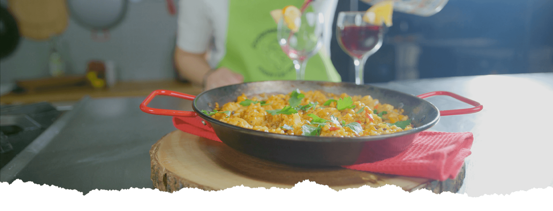 A delicious paella in a black pan, garnished with fresh herbs, placed on a wooden board, accompanied by glasses of wine.